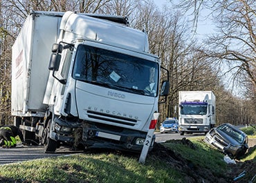 Two commercial trucks and a damaged car at the side of the road after an accident.